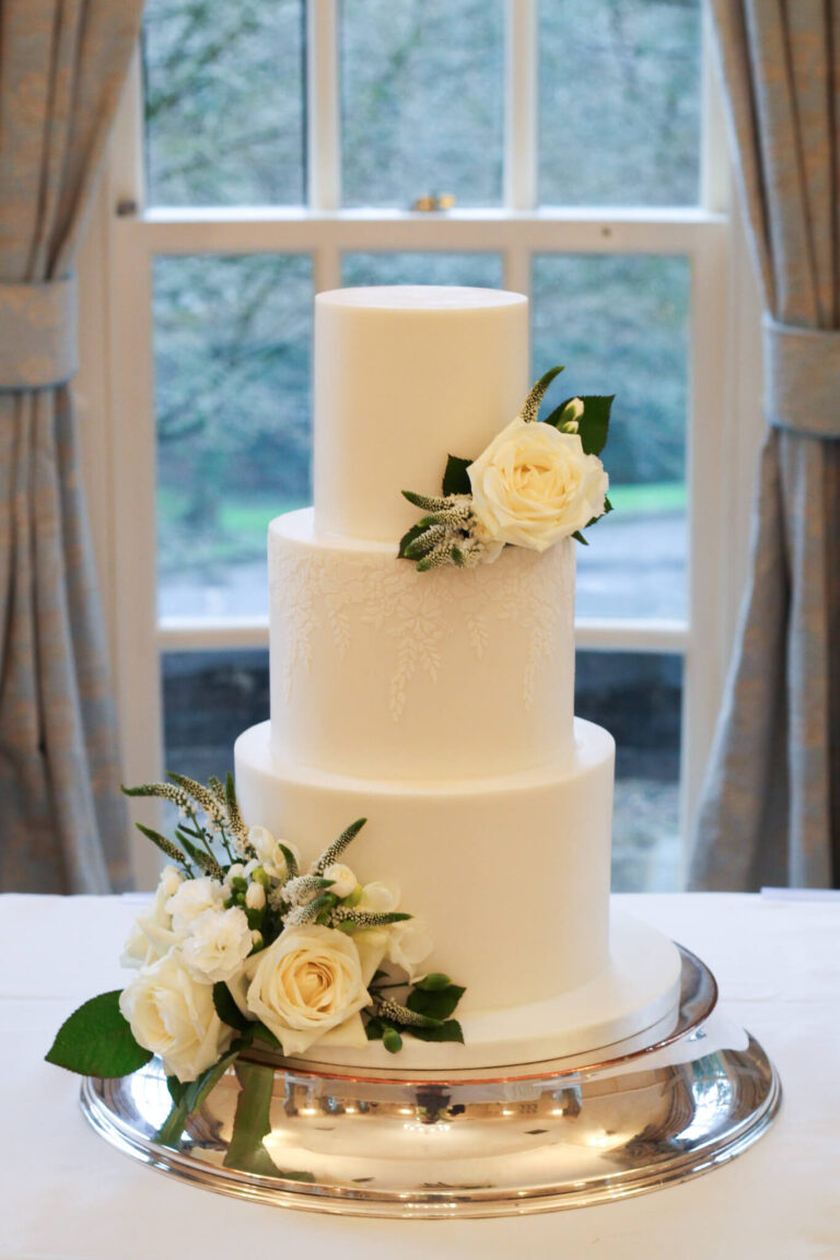 3 tier white wedding cake with delicate stencil detail and fresh white flowers De Courceys Manor